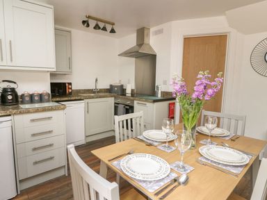 A kitchen with a dining table set for four with plates glasses and cutlery and a vase of purple flowers at Garden View in Llanybydder