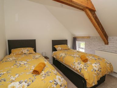 A bedroom with two single beds with yellow floral bedding and wooden beams on the ceiling at Garden View in Llanybydder