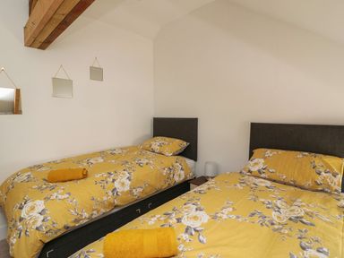 A bedroom with two single beds with yellow floral bedding and three mirrors on the wall at Garden View in Llanybydder