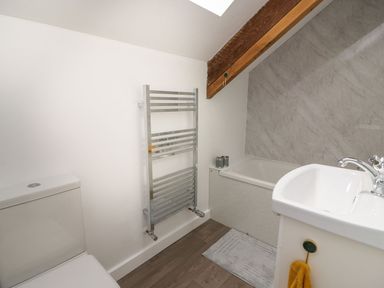 A bathroom with a toilet, heated towel rail, bathtub, sink, and wooden ceiling beam at Garden View in Llanybydder