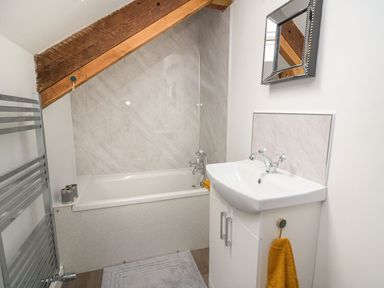 A bathroom with a bathtub a sink with cabinet a mirror and towel rack at Garden View in Llanybydder