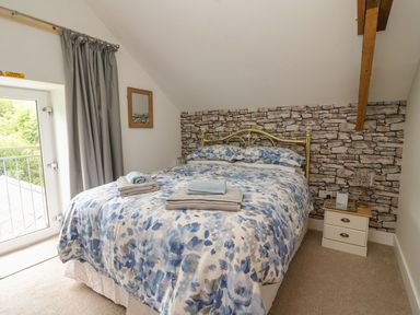 A bedroom with a double bed and floral bedding a nightstand with a lamp a stone pattern wall at Garden View in Llanybydder