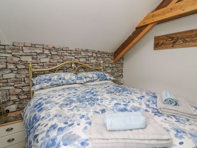 A bedroom with a bed with blue floral bedding and towels on it a stone wall and wooden beam at Garden View in Llanybydder