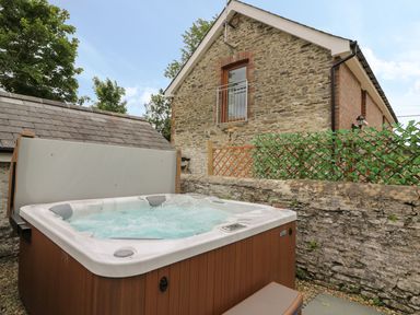 An outdoor hot tub next to a stone wall and a two-story stone house at Garden View in Llanybydder