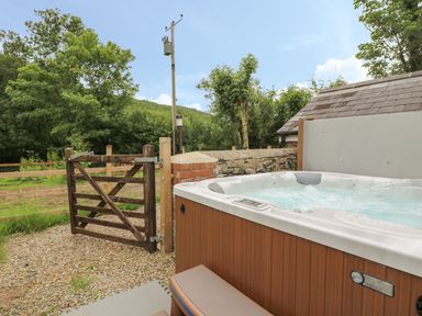 An outdoor hot tub next to a wooden gate and a stone wall with trees in the background at Garden View in Llanybydder
