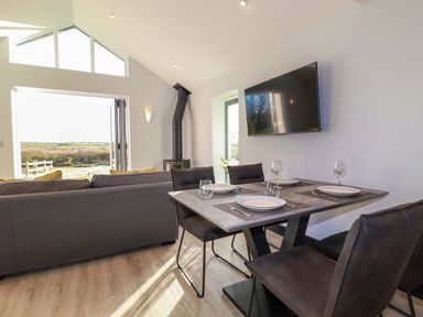 A dining table set for four with plates and glasses next to a gray couch and a wall-mounted TV at Lake View in Kestle Mill near Quintrell Downs