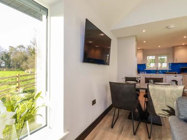 A dining area with a table and chairs next to a kitchen with a washing machine and window at Lake View in Kestle Mill near Quintrell Downs