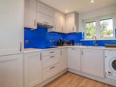 A kitchen with white cabinets blue backsplash and appliances at Lake View Kestle Mill near Quintrell Downs