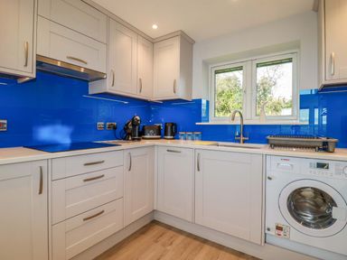 A kitchen with white cabinets blue backsplash and appliances at Lake View in Kestle Mill near Quintrell Downs