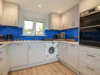 A kitchen with white cabinets blue backsplash a washing machine microwave oven and a window at Lake View in Kestle Mill near Quintrell Downs