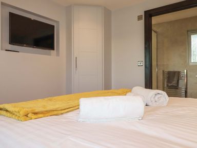A bedroom with a bed and towels with a yellow blanket a wall-mounted tv a door leading to a bathroom at Lake View in Kestle Mill near Quintrell Downs