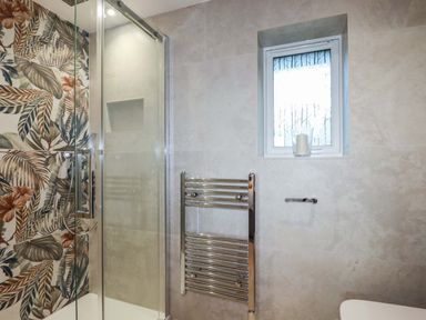 A bathroom with a glass shower enclosure a towel radiator a small window and a candle on the windowsill at Lake View in Kestle Mill near Quintrell Downs