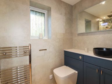 A bathroom with a toilet a countertop with blue cabinets a black basin a towel rail and a window at Lake View in Kestle Mill near Quintrell Downs