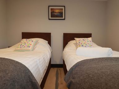 A bedroom with two single beds each with a pillow and blanket and a framed picture on the wall at Lake View in Kestle Mill near Quintrell Downs