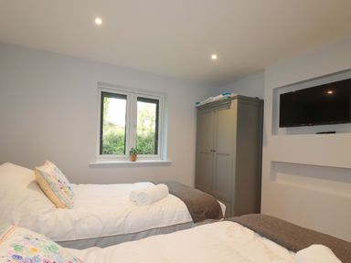 A bedroom with two single beds a wardrobe a window with a plant and a wall-mounted TV at Lake View in Kestle Mill near Quintrell Downs