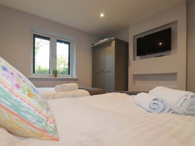 A bedroom with two beds white towels on beds a window a grey wardrobe and a wall mounted TV at Lake View in Kestle Mill near Quintrell Downs