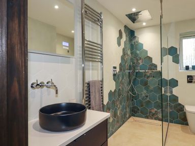 A bathroom with a black round sink a towel rack and a shower with green hexagonal tiles at Lake View in Kestle Mill near Quintrell Downs