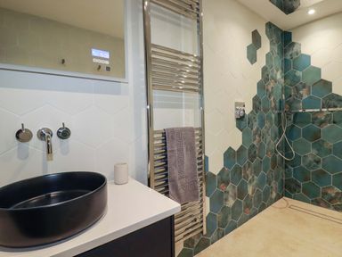 A bathroom with a black sink, digital mirror, towel rail, and hexagonal tiles in white and green at Lake View Kestle Mill near Quintrell Downs
