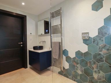 A bathroom with hexagonal tiles a black door a floating vanity with a black basin and a towel radiator at Lake View Kestle Mill near Quintrell Downs