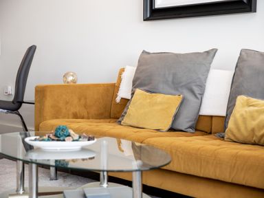 A living room with a yellow sofa a glass coffee table and a black chair at Apartment 17 Abbey Sands in Torquay