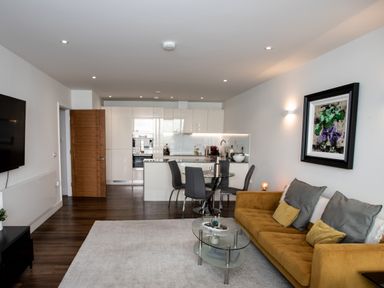 A living room with a mustard sofa and glass coffee table next to a dining area and kitchen at Apartment 17 Abbey Sands in Torquay