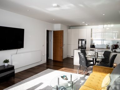A living room with a yellow sofa a glass coffee table a flat screen TV and a dining area with a round glass table and black chairs at Apartment 17 Abbey Sands in Torquay