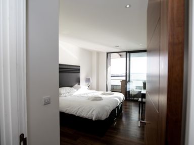 A bedroom with a double bed bedside lamp and glass sliding doors leading to a balcony at Apartment 17 Abbey Sands in Torquay
