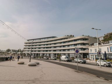 A modern apartment building with balconies along a street with parked cars and a tiled walkway with round stone benches at Apartment 17 Abbey Sands in Torquay