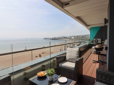 A balcony with chairs a table a small plant and food overlooking the beach and sea at Apartment 17 Abbey Sands in Torquay