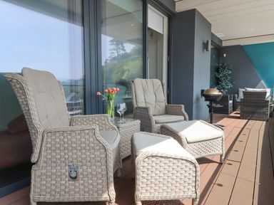 A balcony with wicker chairs ottomans a small table with flowers and wine glasses and a barbecue at Apartment 17 Abbey Sands in Torquay