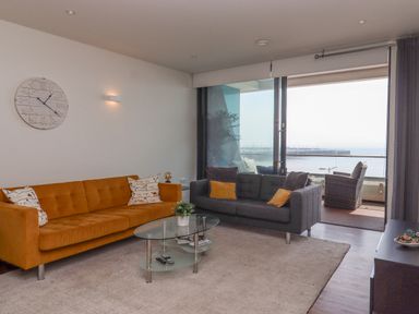A living room with orange and gray sofas glass coffee table and balcony overlooking the sea at Apartment 17 Abbey Sands in Torquay