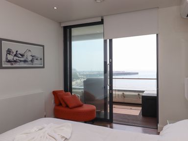 A bedroom with a bed a red chair with cushions a framed painting and a glass door leading to a balcony at Apartment 17 Abbey Sands in Torquay
