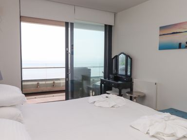 A bedroom with a bed white linens dressing table and sliding glass doors leading to a balcony at Apartment 17 Abbey Sands in Torquay