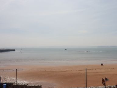 A sandy beach with two people walking near the water and a boat on the calm sea at Apartment 17 Abbey Sands in Torquay