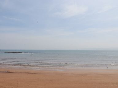 A beach with wet sand and calm sea under a partly cloudy sky at Apartment 17 Abbey Sands in Torquay