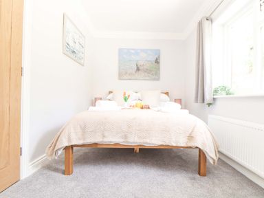 A bedroom with a wooden bed frame beige bedding and a window at Lake View Swanpool Nr Falmouth