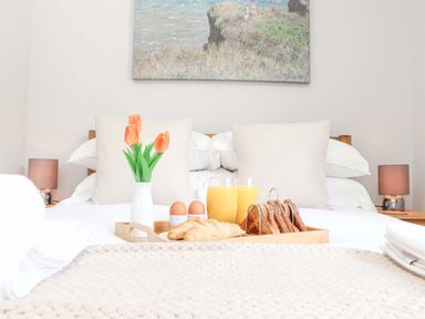 A bed with two pillows breakfast tray with toast croissants eggs orange juice and a vase with tulips at Lake View in Swanpool Nr Falmouth