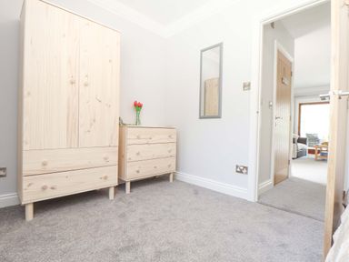 A bedroom with a wooden wardrobe and chest of drawers with flowers on top at Lake View in Swanpool Nr Falmouth