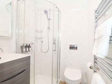 A bathroom with a glass shower enclosure a toilet a wall-mounted sink cabinet and towels at Lake View in Swanpool Nr Falmouth