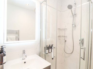 A bathroom with a sink and faucet next to a glass shower enclosure with a showerhead and soap dispensers at Lake View Swanpool Nr Falmouth