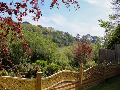 A garden with a wooden curved fence trees and a lake beyond at Lake View in Swanpool Nr Falmouth