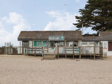 A beach cafe building with a wooden deck and glass railings on a sandy area at Lake View in Swanpool Nr Falmouth