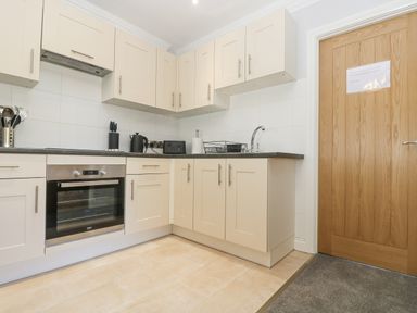 A kitchen with beige cabinets a built in oven a kettle knife block toaster dish rack and wooden door at Lake View Swanpool Nr Falmouth