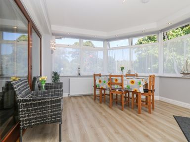 A dining room with a table and six chairs and two wicker chairs near a glass door at Lake View in Swanpool Nr Falmouth