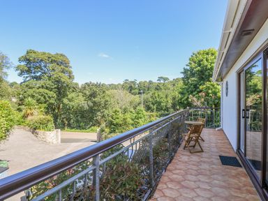 A balcony with two wooden chairs and a table overlooking trees and greenery at Lake View Swanpool Nr Falmouth