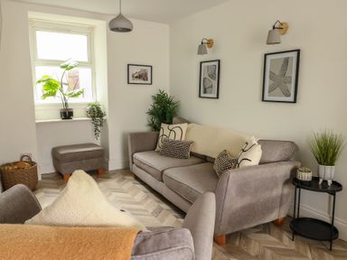 A living room with gray sofas plants and framed pictures at 1 Mona Terrace in Llanfachraeth