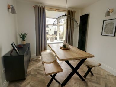 A dining room with wooden table and benches near a window with curtains at 1 Mona Terrace in Llanfachraeth