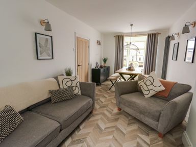 A living room with two gray sofas and a dining table with chairs at 1 Mona Terrace Llanfachraeth