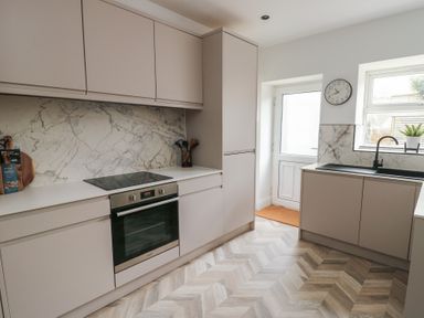 A kitchen with beige cabinets a built-in oven marble backsplash a sink under a window and a door at 1 Mona Terrace in Llanfachraeth