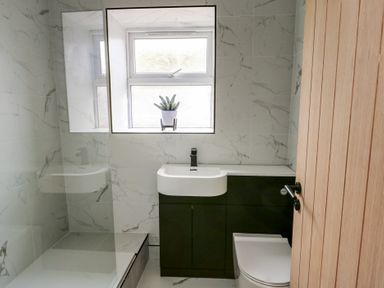 A bathroom with a sink, toilet, shower area, and window with a plant on the sill at 1 Mona Terrace in Llanfachraeth